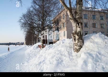 Eine typische Winterszene einer verschneiten Straße am Ufer des gefrorenen Kemijoki-Flusses in Rovaniemi, Finnland Stockfoto