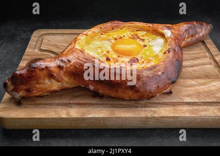 Adjarian khachapuri auf einem hölzernen Brett, auf einem dunklen Hintergrund Stockfoto