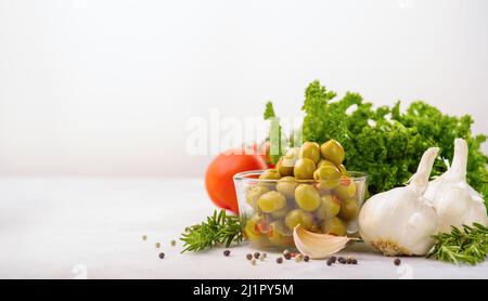 Grüne Oliven, Tomaten, Kräuter, Knoblauch und Pfefferkörner auf weißem Hintergrund. Vitamine, gesunde Bio-Lebensmittel, gesunde Lebensweise. Es gibt freien Speicherplatz für Stockfoto