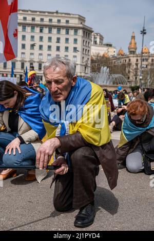 Barcelona, Spanien. 27. März 2022. Ein mit ukrainischer Flagge bedeckter Protestler kniet während der Demonstration. Hunderte von Menschen, hauptsächlich Ukrainer mit Wohnsitz in Katalonien, haben sich auf der Plaza de Catalunya versammelt, um den Widerstand des ukrainischen Volkes gegen die russische Invasion zu unterstützen. Kredit: SOPA Images Limited/Alamy Live Nachrichten Stockfoto