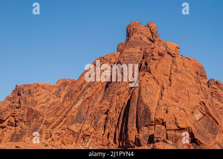 Overton, Nevada, USA - 11. Dezember 2010: Valley of Fire. Roter Felsumhang fällt in senkrechten Linien wie auf der Rückseite der hohen Figur unter blauem Himmel. Stockfoto
