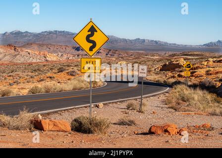 Overton, Nevada, USA - 11. Dezember 2010: Valley of Fire. Schwarze Asphaltstraße schlängelt sich durch breite braune Gebirgswüste Landschaft mit gelb scharfen t Stockfoto