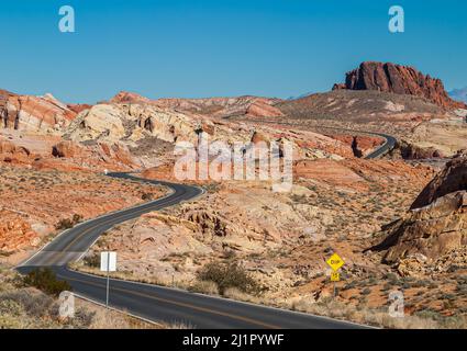 Overton, Nevada, USA - 11. Dezember 2010: Valley of Fire. Breite rot-braun-gelbe felsige Landschaft, die von einer schwarzen asphaltierten Straße von vorne nach hinten geschnitten wird Stockfoto