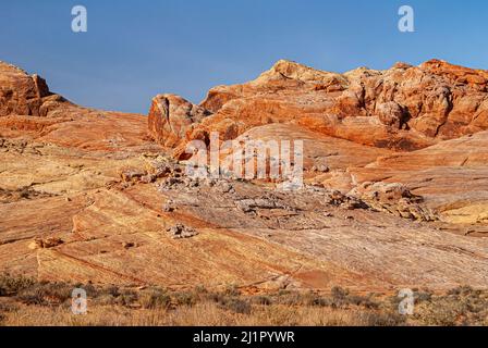 Overton, Nevada, USA - 11. Dezember 2010: Valley of Fire. Schräges rot-braun-gelbes Felsplateau, das wie zwischen felsigen Hügeln unter blauem Himmel fließt. Stockfoto