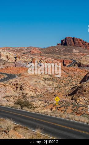 Overton, Nevada, USA - 11. Dezember 2010: Valley of Fire. Breite rot-braun-gelbe felsige Landschaft, die von einer schwarzen asphaltierten Straße von vorne nach hinten geschnitten wird Stockfoto