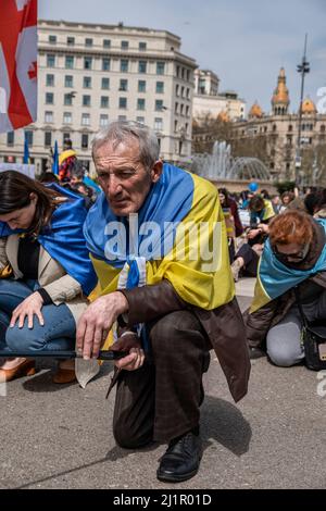 Barcelona, Spanien. 27. März 2022. Ein mit ukrainischer Flagge bedeckter Protestler kniet während der Demonstration. Hunderte von Menschen, hauptsächlich Ukrainer mit Wohnsitz in Katalonien, haben sich auf der Plaza de Catalunya versammelt, um den Widerstand des ukrainischen Volkes gegen die russische Invasion zu unterstützen. (Foto von Paco Freire/SOPA Images/Sipa USA) Quelle: SIPA USA/Alamy Live News Stockfoto