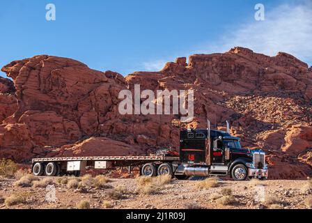 Overton, Nevada, USA - 11. Dezember 2010: Valley of Fire. Nahaufnahme von Tieflader und rot-schwarzen Kel-West-LKW-Fahrten vor dem Red Rock Mountain Stockfoto