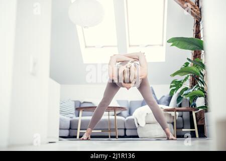 Junge schöne Schwangerin, die zu Hause in ihrem Wohnzimmer Pilates trainiert. Gesunder Lebensstil und aktives Konzept für Schwangerschaft und Mutterschaft. Stockfoto