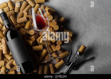 Originalkomposition. Eine Flasche Wein, ein Weinglas und ein Korkenzieher liegen auf Weinkorken. Isoliert auf grauem Hintergrund. Es ist freier Speicherplatz zum Einfügen vorhanden. Stockfoto