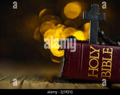 Auf einem Holztisch stehen eine Heilige Bibel und ein katholisches Kreuz auf einem hellgelben Hintergrund. Auf dem Foto befinden sich keine Personen. Es gibt freien Platz für mich Stockfoto