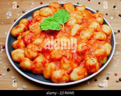 Traditionelle hausgemachte italienische Gnocchi in aromatischer Tomatensauce auf einem dekorativen Teller serviert und mit Kräutern, Basilikum, farbigem Pfeffer, Knoblauch und garniert Stockfoto