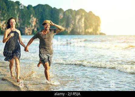 Unsere Dosis von Vitamin Meer zu bekommen. Aufnahme eines glücklichen jungen Paares, das die Hände hält, während es am Strand entlang läuft. Stockfoto