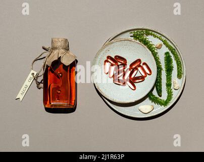 Glasflasche mit Algenöl, Gelatinkapseln und lebenden Algen in Tontellern. Transparenter Behälter ist mit Jute-Faden mit Holzetikett gebunden. Braun Stockfoto