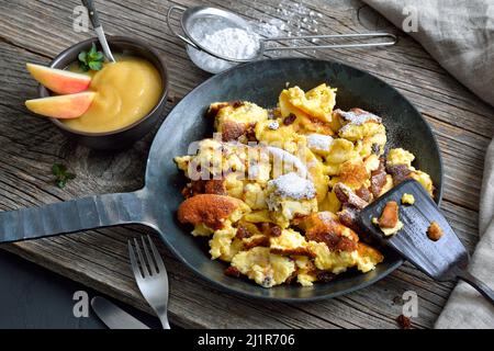 Traditioneller Wiener Kaiserschmarrn, geschredderte süße Pfannkuchen mit Rosinen, serviert in einer eisernen Bratpfanne auf alten Holzbrettern auf einem Schieferteller Stockfoto