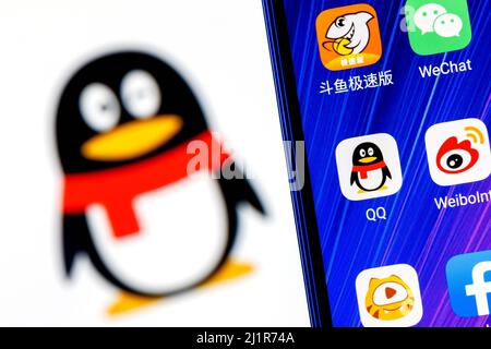 Das Symbol der chinesischen Nachrichtendienst-Anwendung Tencent QQ unter anderem auf dem Smartphone-Bildschirm. Auf dem Hintergrund ist das QQ-Logo zu sehen. Stockfoto