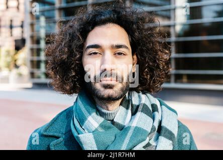 Stadtportrait des jungen lockigen Mannes mit Bart auf der Straße posiert Stockfoto