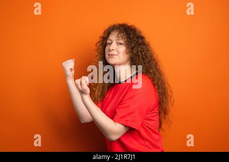 Bild von ziemlich rothaarige weibliche Fan in Sport-Fußball-Uniform halten die Fäuste für ihren Fußball-Team-Sieg, menschliche Emotionen Konzept. Stockfoto