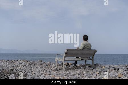Deprimierter einsamer Mann, der auf einem Ufer am Meer sitzt. Stockfoto