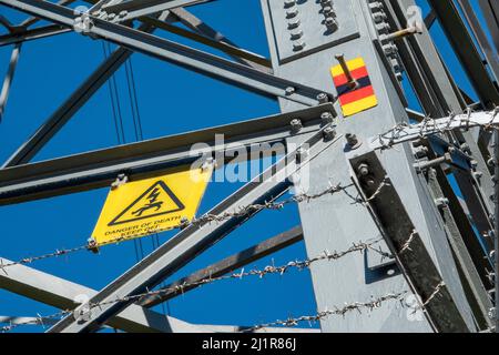 Unterer Abschnitt eines Sendeturms mit Warnschild „Gefahr des Todes“ und kletterfester Stacheldraht-Barriere gegen einen blauen Himmel Stockfoto