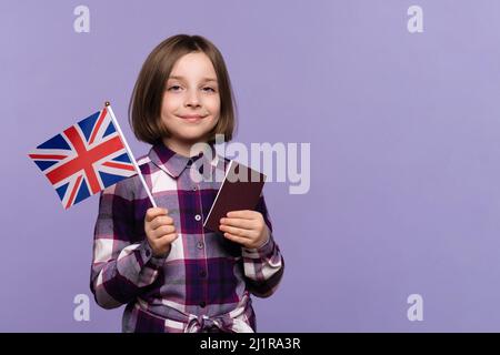 Kind Mädchen 9-11 Jahre alt in Karabinerkleid mit Blick auf die Kamera. Schulmädchen mit Pass und UK-Flagge auf lila Hintergrund, Kopierer Raum, Einwanderung..Study Abroad Konzept. Stockfoto