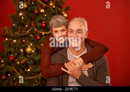 Diese gehen auf ihre Weihnachtskarte. Ein zugeschnittenes Porträt eines glücklichen reifen Paares vor einem Weihnachtsbaum. Stockfoto