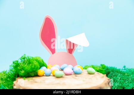 Das rosa Kaninchen versteckt sich hinter einem Stumpf. Ostern Grußkarte mit Ostersymbolen. Stockfoto