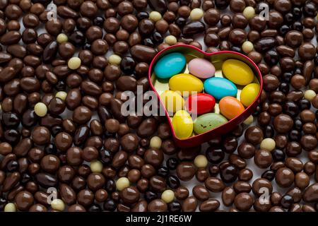 Bunte Mandel-Schokolade Süßigkeiten in Metall, herzförmige Box, auf der dunklen Kugel Schokolade Hintergrund.Draufsicht Stockfoto