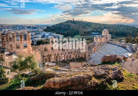 Sonnenuntergang über dem Odeon des Herodes Atticus, gelegen am Südwesthang der Akropolis, in Athen, Griechenland. Filopappos Hill mit dem Filopappos monu Stockfoto