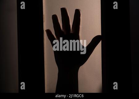 Silhouette der Hand. Frau Hand hinter dem Milchglas als Symbol für Hilfe oder Gefahr. Gewalt gegen Frau Konzept Idee Hintergrund. Stockfoto