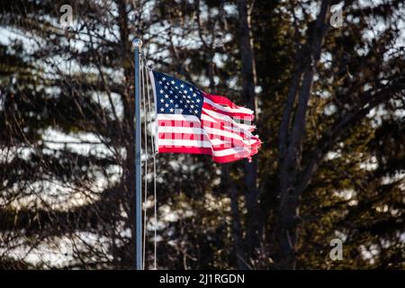Schlecht zerfetzte amerikanische Flagge, die von der Fahnenstange außen, horizontal, fliegt Stockfoto