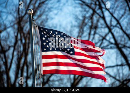 Nahaufnahme einer schwer zerfetzten amerikanischen Flagge, die von der Fahnenstange draußen, horizontal, fliegt Stockfoto
