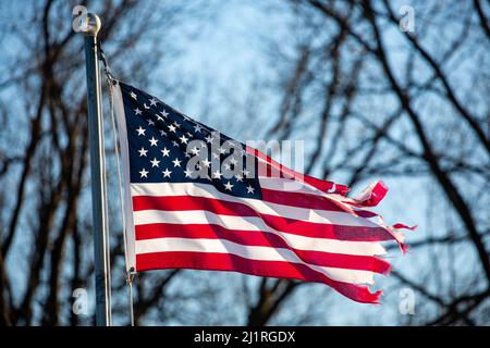 Nahaufnahme einer schwer zerfetzten amerikanischen Flagge, die von der Fahnenstange draußen, horizontal, fliegt Stockfoto