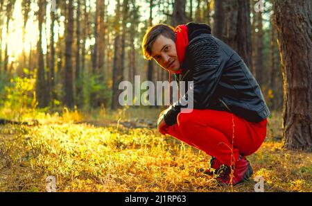 Ein junger, gutaussehender Mann in einem roten warmen Anzug und einer Lederjacke sitzt auf deinen Spukschwärmen Stockfoto
