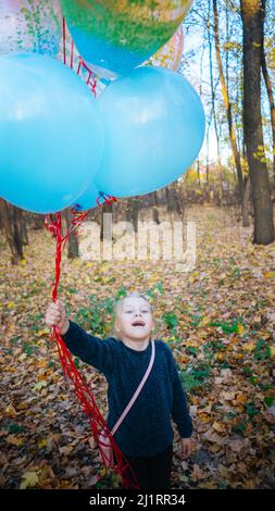 Ein Kind geht mit bunten Kugeln durch den Wald. Mädchen hält farbige Ballons in der Hand Stockfoto