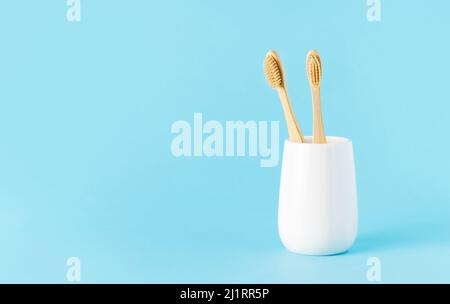 Set aus natürlichen Bambus-Zahnbürsten aus Keramikglas auf blauem Hintergrund. Umweltfreundliches, abfallfreundliches Konzept. Platz für Text kopieren, selektiver Fokus Stockfoto