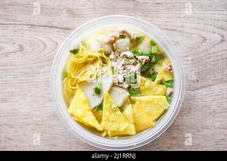 Nudeln Schweinebälle Fischbällchen und gehacktes Schweinefleisch mit knusprigen Wontons und Gemüse in Kunststoffschale auf Holztisch, Draufsicht Thai und China Asiatische Küche de Stockfoto