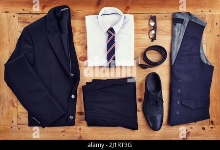 Heben Sie sich am Arbeitsplatz mit diesem stilvollen Outfit hervor. Ein elegantes Business-Outfit, das auf einem Holztisch ausgelegt ist, in einem hohen Winkel. Stockfoto