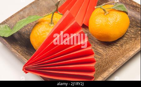 Chinesisches Neujahr, Komposition mit Mandarinen, lustiges Origami aus rotem Papier auf einem dunklen Holzteller auf weißem Grund. Stockfoto