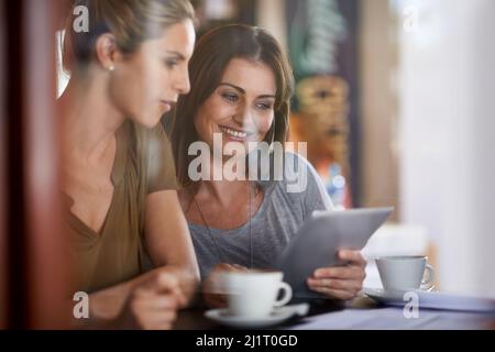 Technologie bringt Menschen näher. Zwei junge Frauen, die in einem Café ein Tablet betrachten. Stockfoto