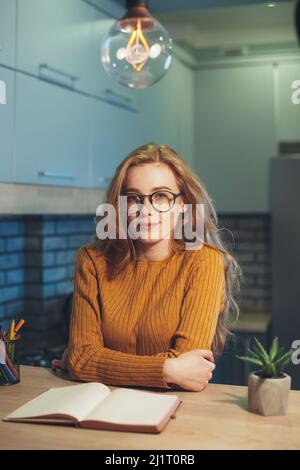 Müde rothaarige Studentin sitzt an einem Tisch mit Lehrbüchern Blick auf Kamera Vorbereitung für College-Prüfungen. Wunderschönes Porträt. Bildung Stockfoto