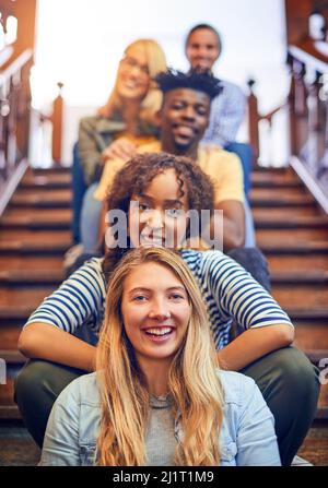 Alle auf dem Weg in eine bessere Zukunft. Porträt einer Gruppe verschiedener Studenten, die in einer Reihe auf der Treppe auf dem Campus sitzen. Stockfoto