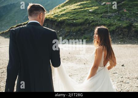 Die Braut und der Bräutigam waren an ihrem Hochzeitstag auf dem Sand an einem See spazieren gegangen. Paar Hochzeit posiert. Stockfoto