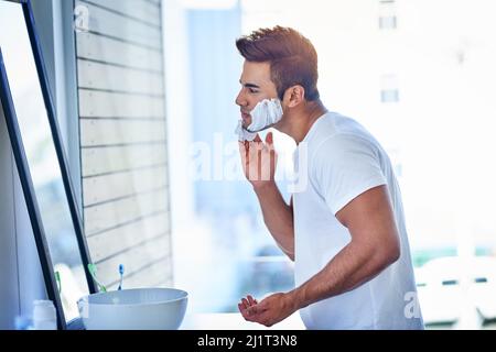 Alles abheben. Aufnahme eines hübschen jungen Mannes, der sich im Badezimmer seine Gesichtshaare rasiert. Stockfoto