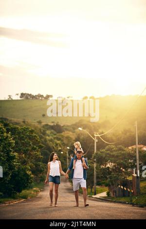 Genießen Sie die einfachen Dinge mit denen, die Sie lieben. Aufnahme einer jungen Familie, die draußen die Straße entlang spazieren geht. Stockfoto