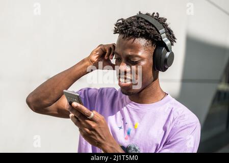 Schwarzes männliches Modell mit Kopfhörern und Musikgenuss. Tragen eines violetten Hemdes mit Telefon in der Hand. Stockfoto