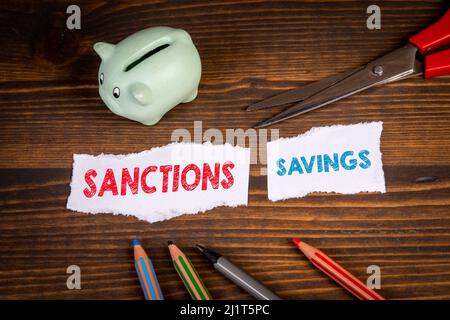 Wirtschaftssanktionen und Sparkonzept. Schneiden Sie Papier, Schere und Sparschwein auf einem hölzernen Hintergrund. Stockfoto