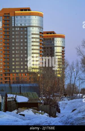 Neue und alte Häuser am Abend. Mehrstöckige neue Gebäude in der Nähe von alten Slums im Winter. Nowosibirsk, Sibirien, Russland, 2022 Stockfoto