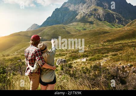 Wir haben einen langen Weg zurückgebracht und sind sogar noch weiter gegangen. Rückansicht eines jungen Paares, das einen Bergblick in der Natur bewundert. Stockfoto