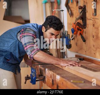 Details machen den Unterschied. Aufnahme eines fokussierten Handwerkers, der während der Arbeit in seiner Werkstatt ein Stück Holz misst. Stockfoto