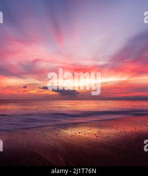 Ein hochauflösender Sonnenuntergang im Ozean mit Sonnenstrahlen, die durch die Wolken brechen, im vertikalen Bildformat Stockfoto